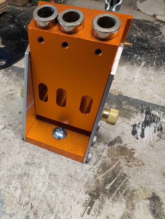 Orange pocket hole jig med tre hål och skruvar på en arbetsbänk.