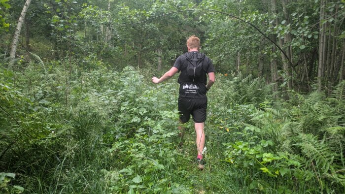 Person springer genom grönskande skog med ryggsäck, omgiven av tät vegetation och träd.