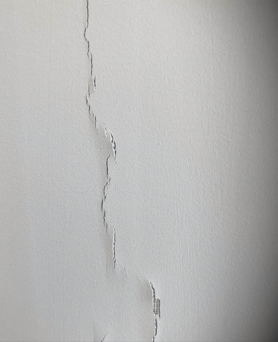 Sprickor i lodrät gipsvägg i friggebod, synliga längs spacklade skarvar med glasfiberremsor.