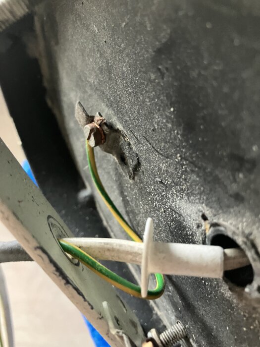 Taklampa med jordad gul och grön sladd ansluten till en metallplatta, synlig skruv och ledningar mot mörk bakgrund.