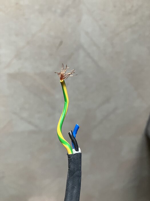 Närbild av tre elkablar: en gul/grön för jord, en blå för neutral och en svart för fas, visas med lösa ändar för inkoppling.