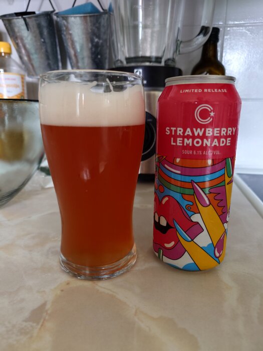 Ett glas med skummande rödöl bredvid en burk "Strawberry Lemonade Sour" på ett köksbord.