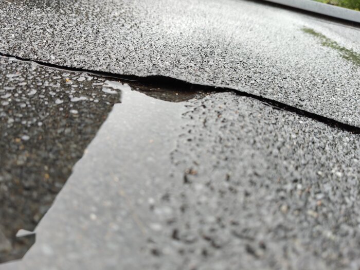 Vattenpöl på ett vågigt garagepapptak med synlig glipa där vatten samlas.