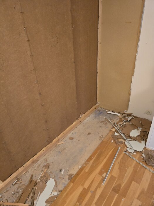 Vägg som delvis rivits ner, med byggmaterial och bitar av gips på golvet, redo för renovering eller ombyggnad.