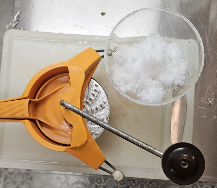 En orange ishyvlare bredvid en glasbägare med krossad is, använd för att göra Frozen Margarita.