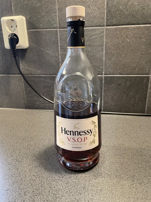 Flaska med Hennessy V.S.O.P cognac på en köksbänk framför grå kakelvägg.