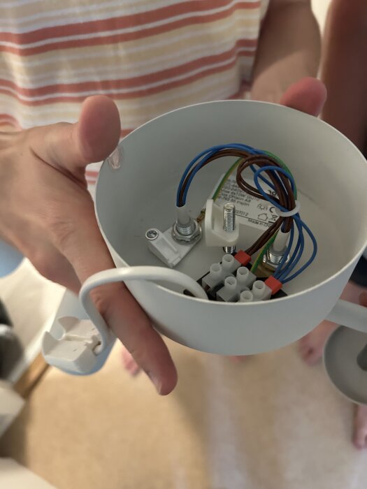 Person håller en takdosa med elsladdar och skruvhål för lampmontering, cirka 7 cm mellan skruvhålen.