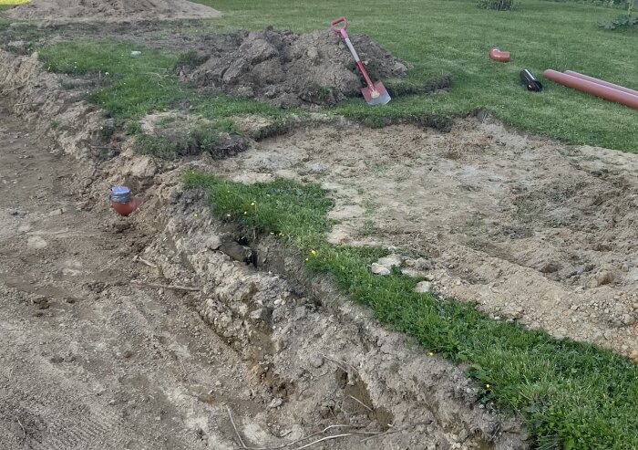 Grävt hål i trädgård med rör och jordhögar bredvid. Röd spade och grönt gräs syns i bilden.