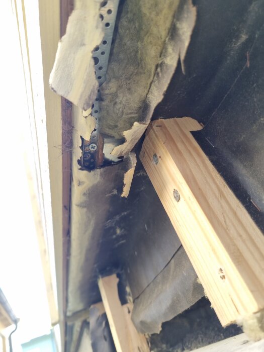 Träreglar och rivet fuktpapper exponerat på en vägg under renovering, med metallbeslag och isoleringsmaterial synliga.