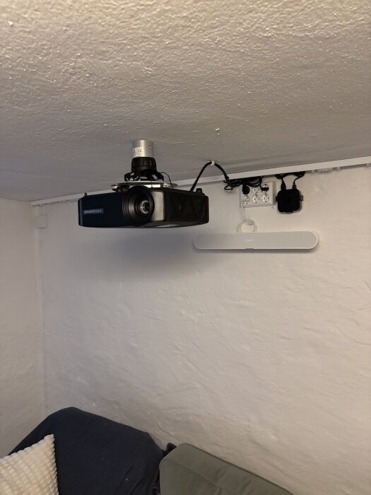 Takmonterad projektor och eluttag med sex uttag på väggen, del av en hemmabioinstallation.