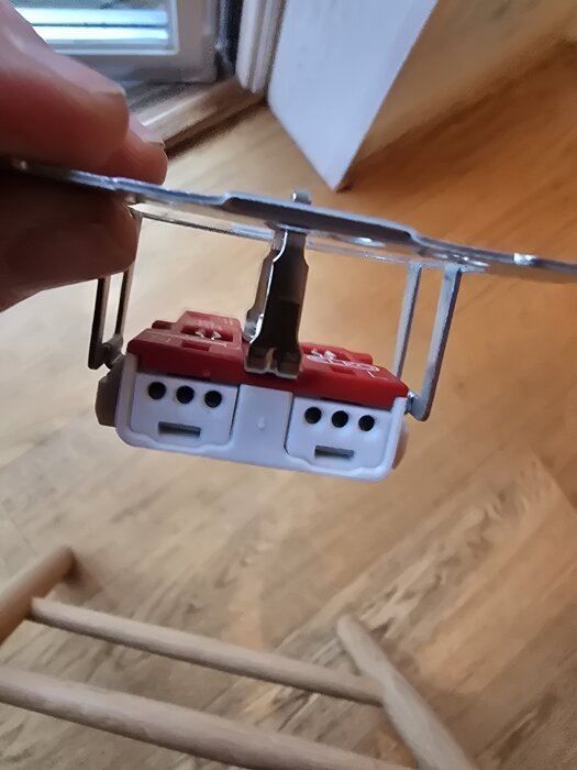 Bild på ett nytt eluttag utan de förväntade skruvarna för kabelinstallation, hålls i en hand bredvid ett fönster.