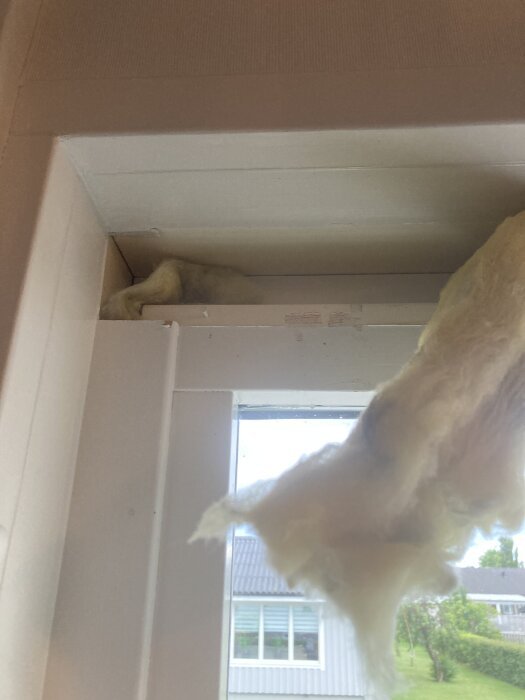 Närbild av ett fönsterparti med en borttagen bräda och utsatt isolering i ett elementhus från 70-talet.