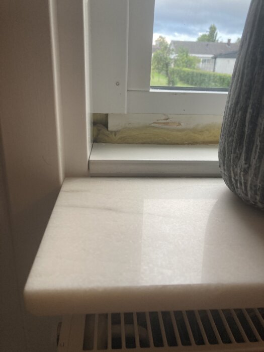 Närbild av fönsterkarm med borttagen smygebräda, isolering synlig i mellanrummet.