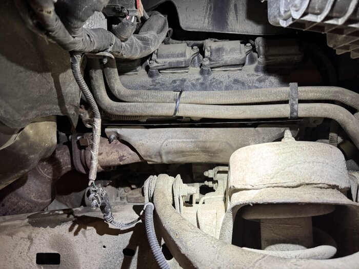 Bilens undersida med headers och avgassystem, synligt damm och smuts på komponenterna, indikerar nyligen utfört arbete på rören.