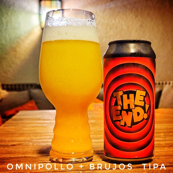 Glas med skumfylld öl bredvid en burk med "The End!"-design på ett träbord.