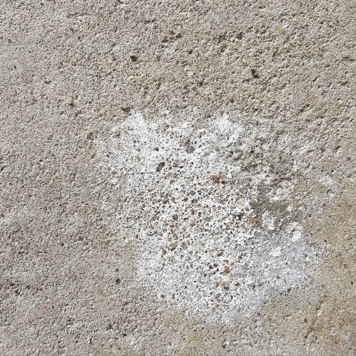 Fläck på betonggolv i garage med vit kalkavlagring.