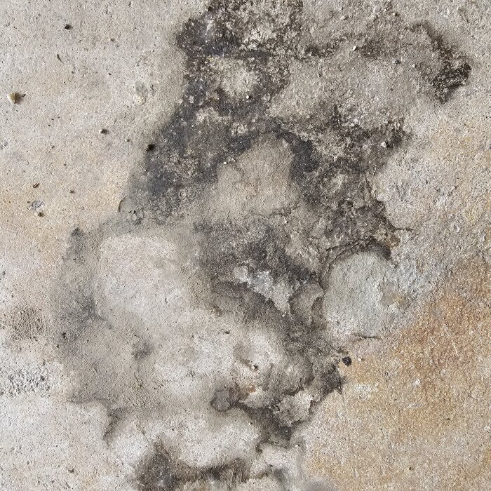 Fläckar och missfärgningar på garagegolvets betongyta, med mörka och ljusa områden som sprider sig.