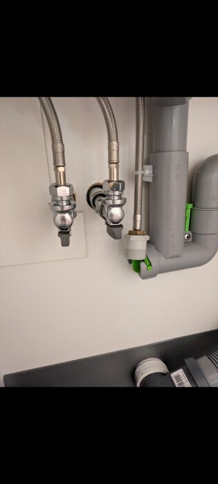 Diskmaskinsinstallation med avloppsslangar och rör, visar anslutningar med olika dimensioner under diskbänken.