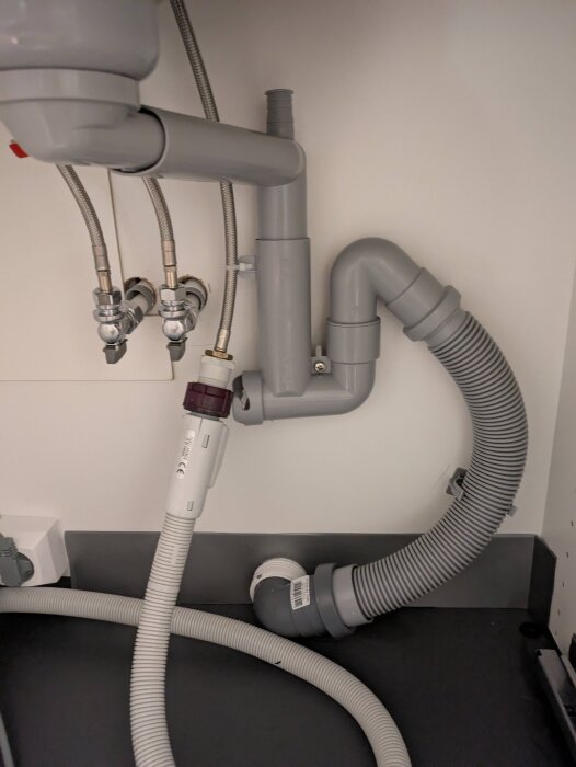Diskmaskinens avloppsslang och rör under diskbänken med olika dimensioner, vilket orsakar installationsproblem.