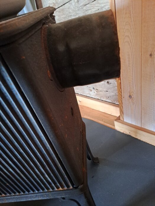 Kamin JØTUL 602 N med stödben sedd från sidan, monterad mot en vägg av trä.