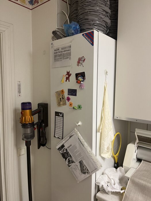 Vit enhet med klistermärken och dokument i tvättstuga, text "Temovex" synlig. En dammsugare monterad på väggen bredvid.