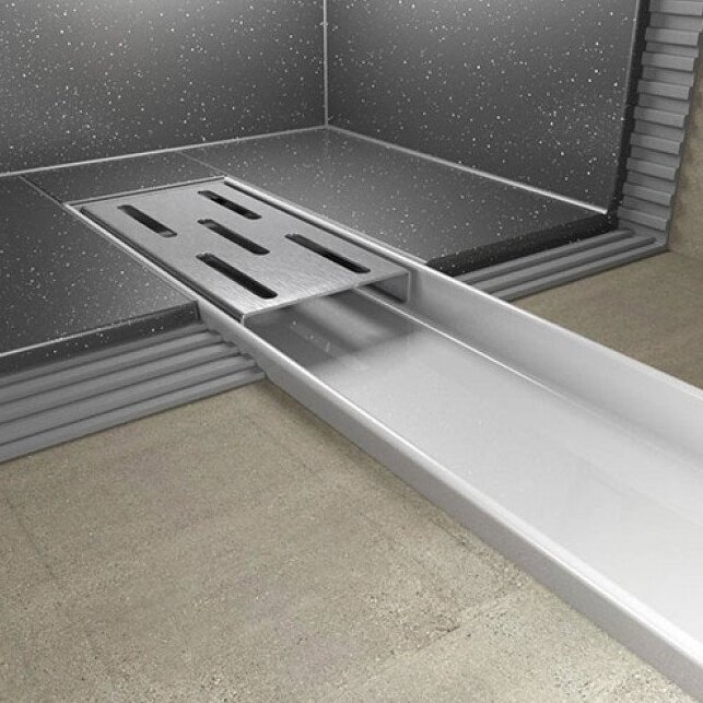 Avlång duschbrunn med metallgaller och kant, installerad i ett badrum med kaklade väggar och golv.