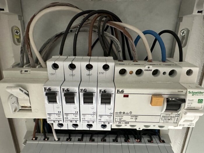 Bild på en normcentral med flera brytare och anslutna kablar i olika färger. Kablarna är svart, brun och vit samt blå och svart.