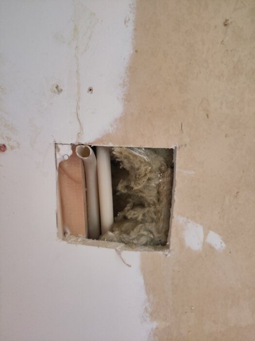 Hål i väggen med exponerade rör och isolering, del av renoveringsprojekt för värmepumpinstallation.