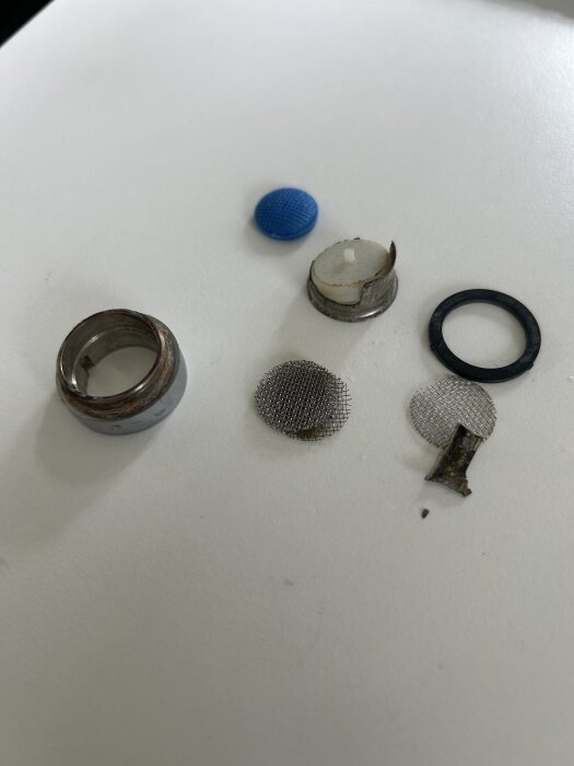 Delar från en strålsamlare inklusive en trasig hylsa, nät och packning ligger utspridda på en vit yta.