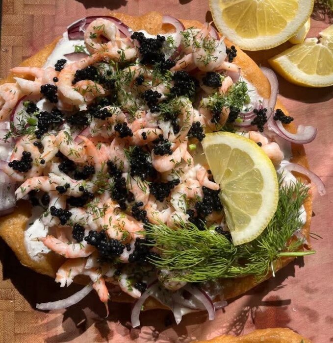 Lyxlangos toppad med räkor, svart kaviar, dill, rödlök och citronskivor på ett bröd.