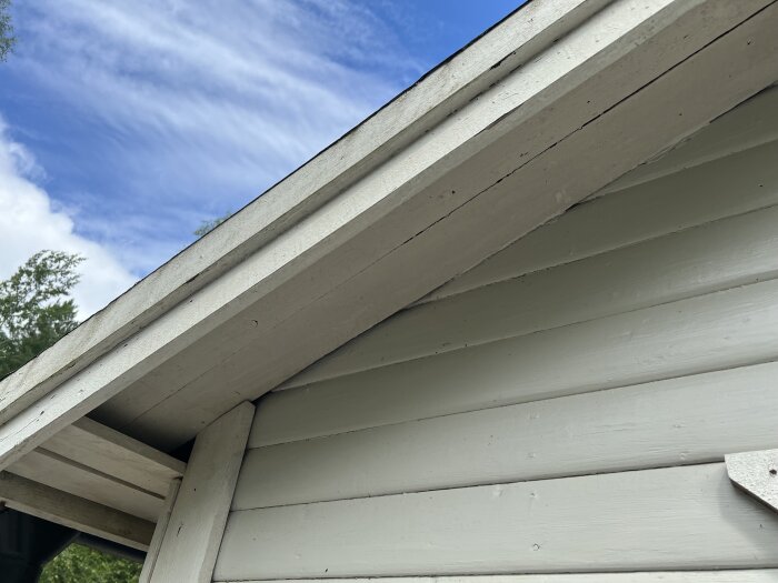 Springor mellan fasad och vindskivor på en byggnad under blå himmel; potentiellt inträde för getingar.