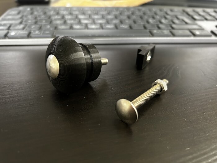 3D-printad krok för handdukstork liggande på svart bord, med tillhörande skruv och mutter synliga i bilden.