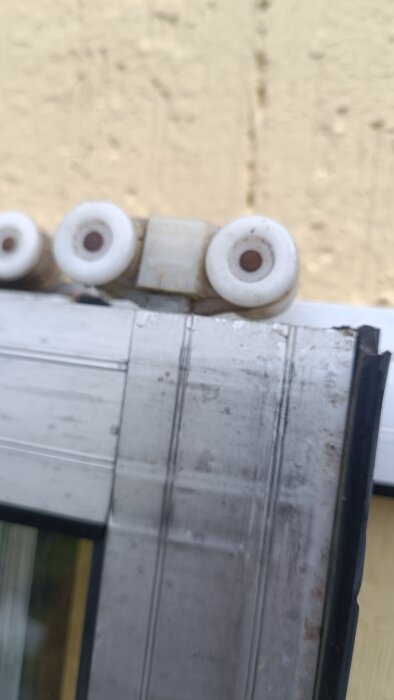 Närbild på en skjutdörrs rullar med slitet material; tre vita hjul syns mot en ljus bakgrund.