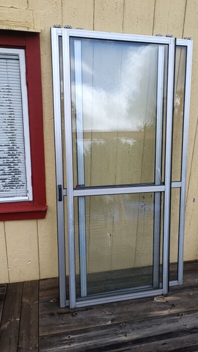 Glasdörr med träpanel och röd kant, stående uppställd på en trätrall, möjligtvis en skjutdörr med metallram.