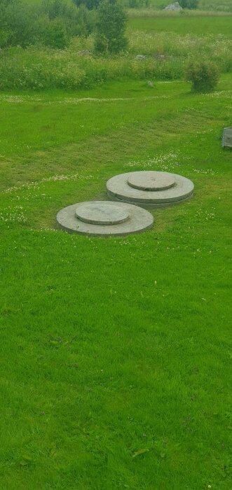 Två betongbrunnslock synliga på en gräsmatta, ett något mindre placerat framför ett större.