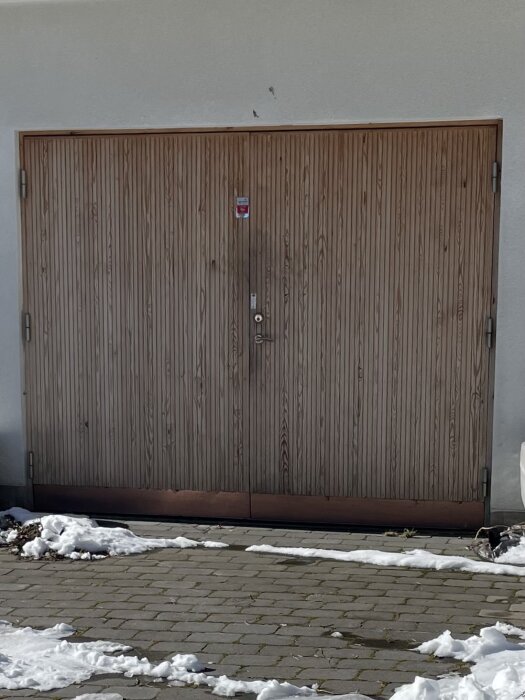 Garageport med smala vertikala träpaneler och distans, omgiven av snö och plattor.