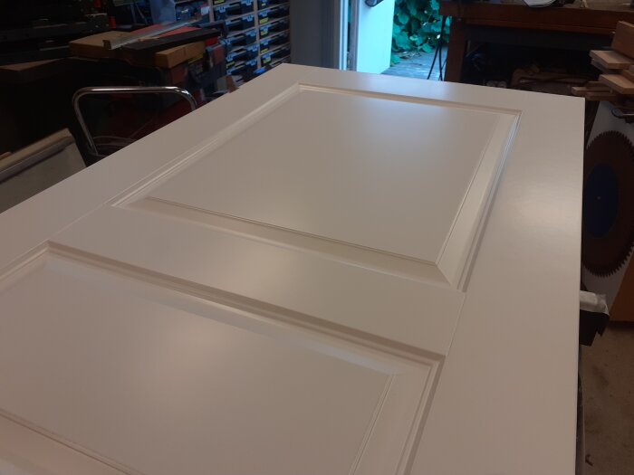 Nymålad vit dörr i ett dammigt garage med verktygshyllor i bakgrunden, resultatet blev över förväntan trots dåliga förutsättningar.