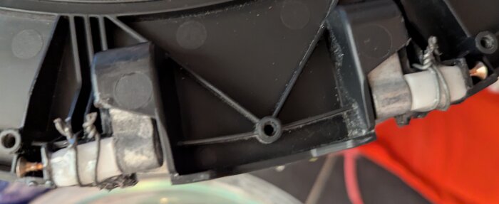 Reparerad svart plastdel med gångjärn och skruvar på en tvättmaskinslucka, lagad med lim.