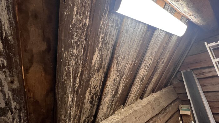 Kattovintti, jossa näkyy vanhat lautapaneelit, tikkaat ja kirkas loisteputkivalaisin.