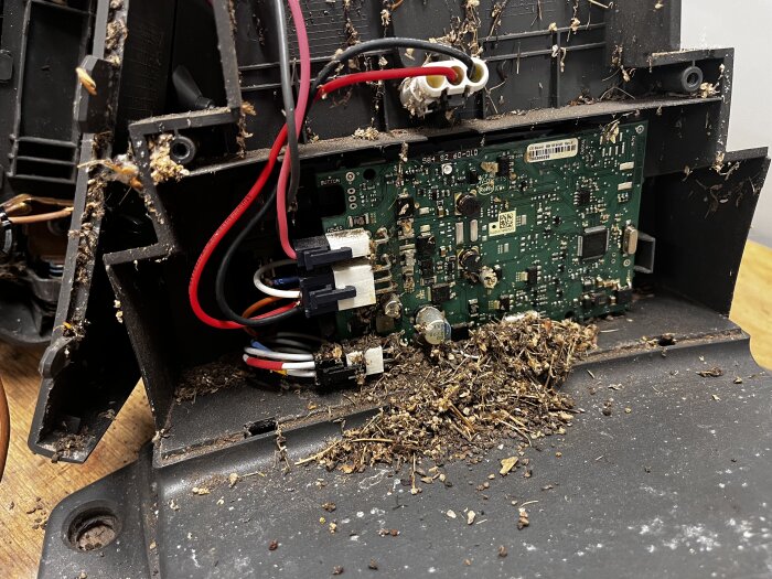 Öppen laddstation med elektroniska komponenter, invändigt täckt av smuts och rester, som ser ut som delar av ett myrbo.