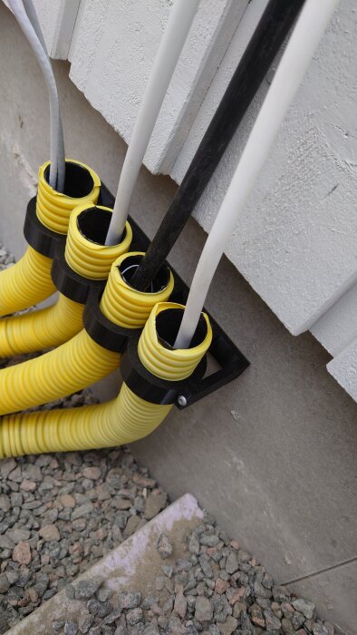 Gula och svarta 50mm hållare för elrör monterade på en vägg, gjorda av PETG, med kablar och grus på marken.