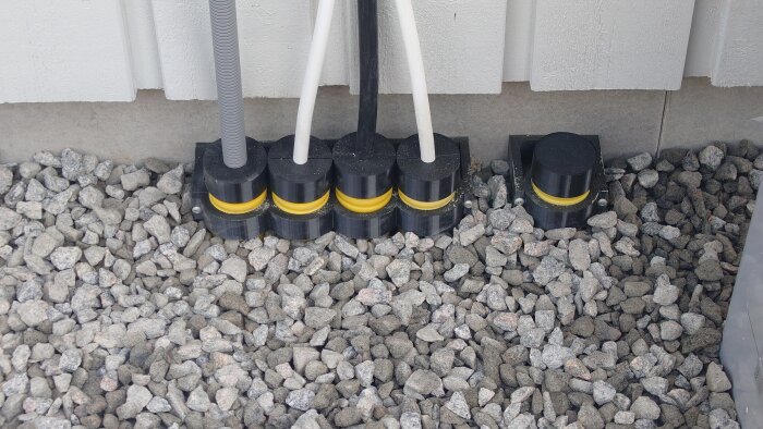 Självgjorda 50mm hållare i PETG för elrör, placerade på mark av grus, med svarta och gula delar, intill en byggnadsvägg.