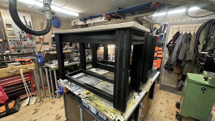 Svart målat underrede till arbetsbänk i verkstad med verktyg hängande på väggar och hyllor runtomkring.