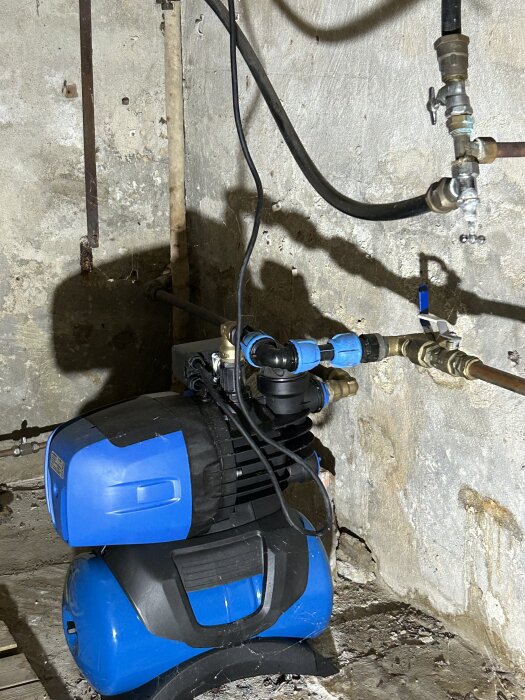 Vattenpump a-collection PA-1850 installerad i en källare med kopplingar och slangar anslutna till en vägg.