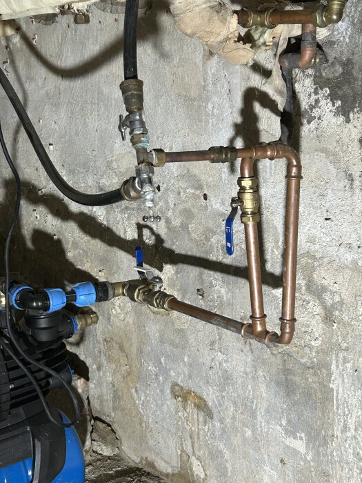 Vattenpump och rörsystem monterade i en källarvägg, del av en privat brunnsanläggning.