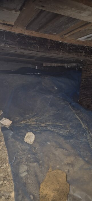 Plasttäckning över marken i en grund med träbjälkar i taket, förberett för byggprojekt i källare.