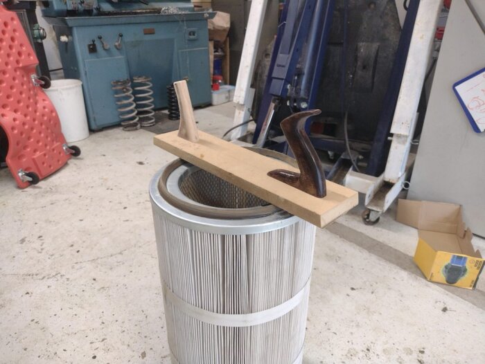 Slipblock med två grepp, ett av trä och ett lackerat, placerat över ett större metallfilter i en verkstadsmiljö.