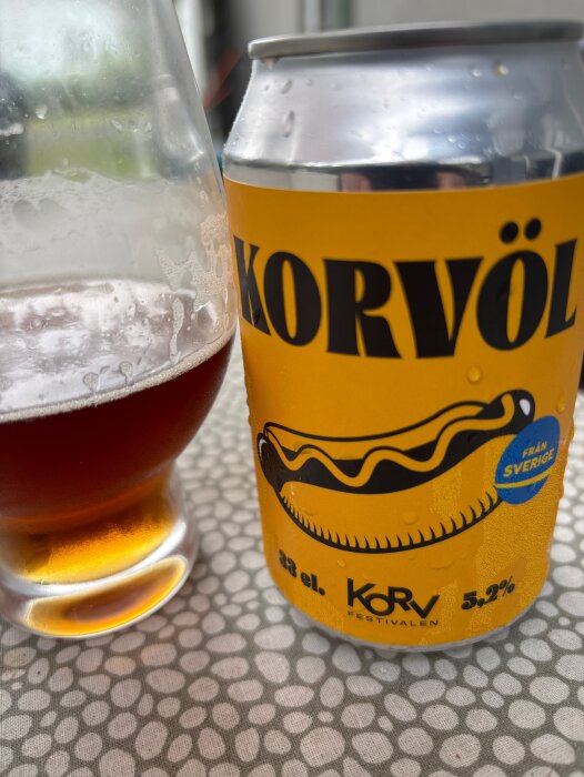 Öppen burk med "Korvöl" och ett glas med mörk lageröl på ett bord.