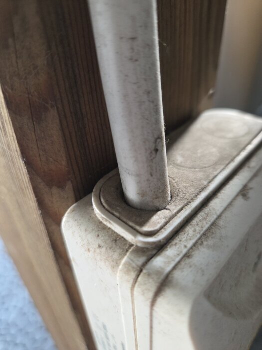 Säkerhetsbrytare monterad utomhus med en vit kabel, delvis täckt av smuts, invid en trävägg.