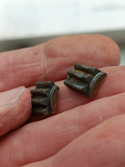 Brutet kugghjul från ett fönster visas liggandes på en hand.